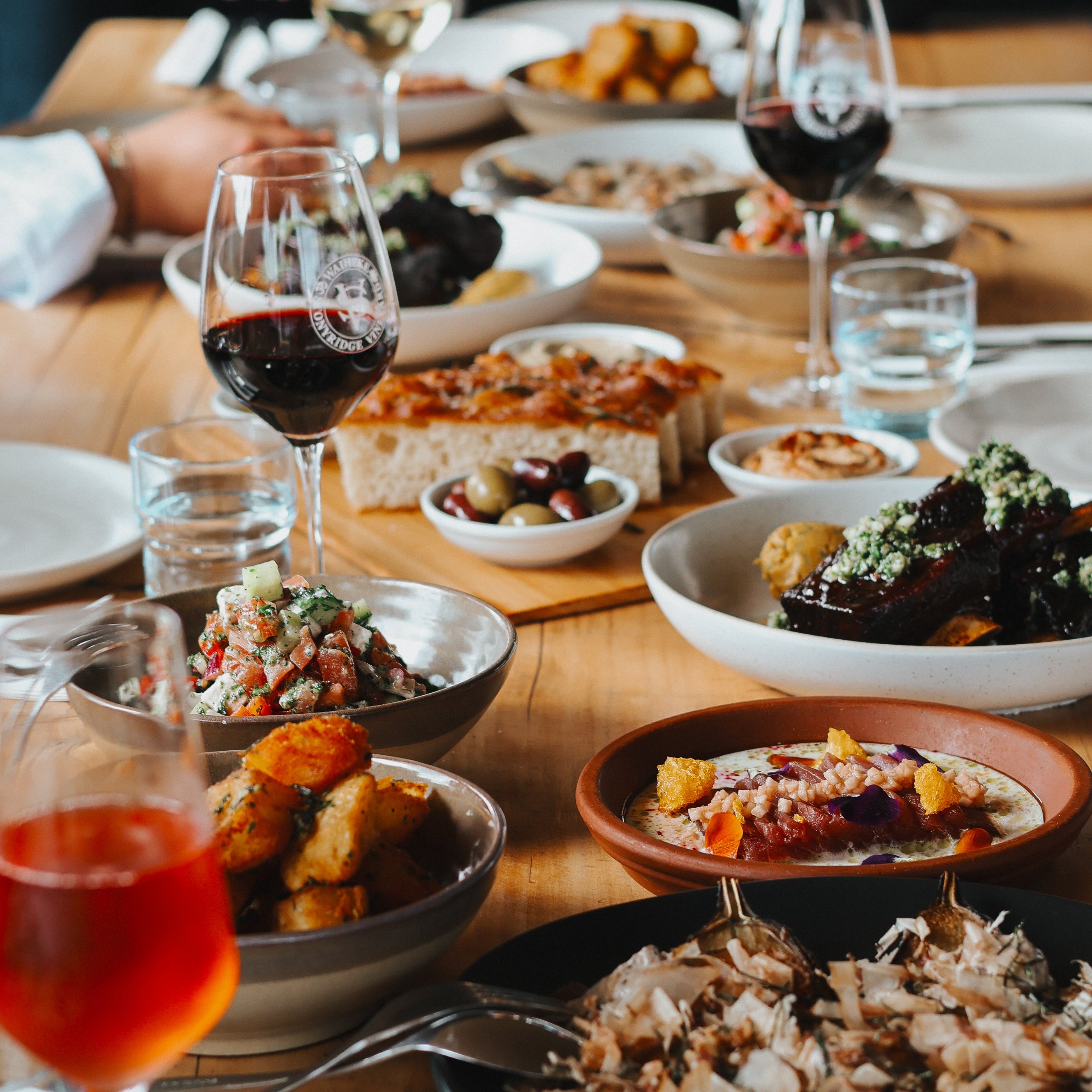 Dinner table with various dishes and wine glasses, people in the background